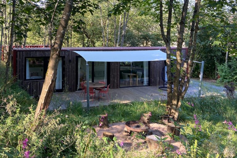 Modernes Seecontainer Tiny House im Grünen mit Terrasse und Überdachung.